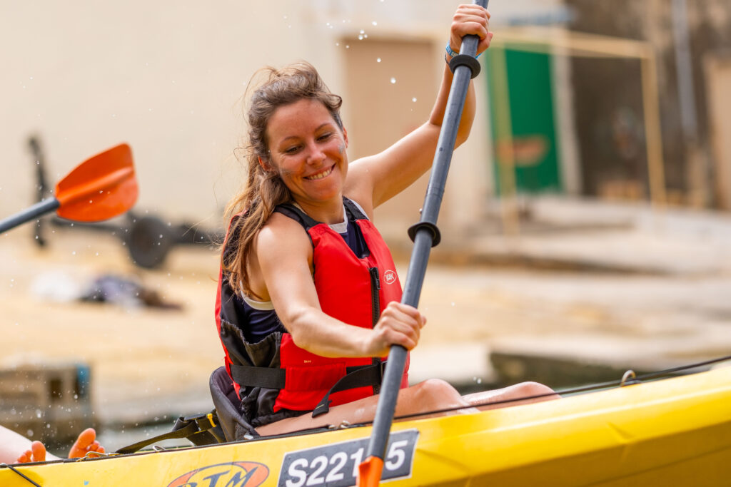 Femme qui sourie et qui rame lors d'une sortie kayak à Dwerja Bay à l'occasion d'une visite sur l'île de Gozo