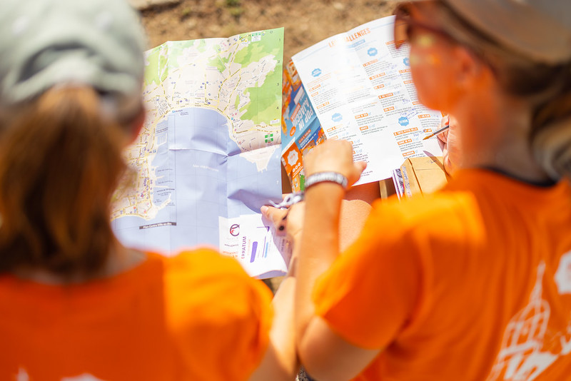 Femmes de dos avec un t-shirt orange qui déchiffrent une carte d'Ajaccio lors de leur visite de la ville